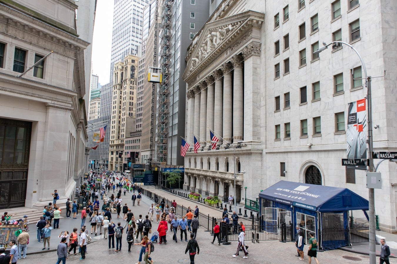 The New York Stock Exchange building on Wall Street with US flags on its facade and pedestrians on the street