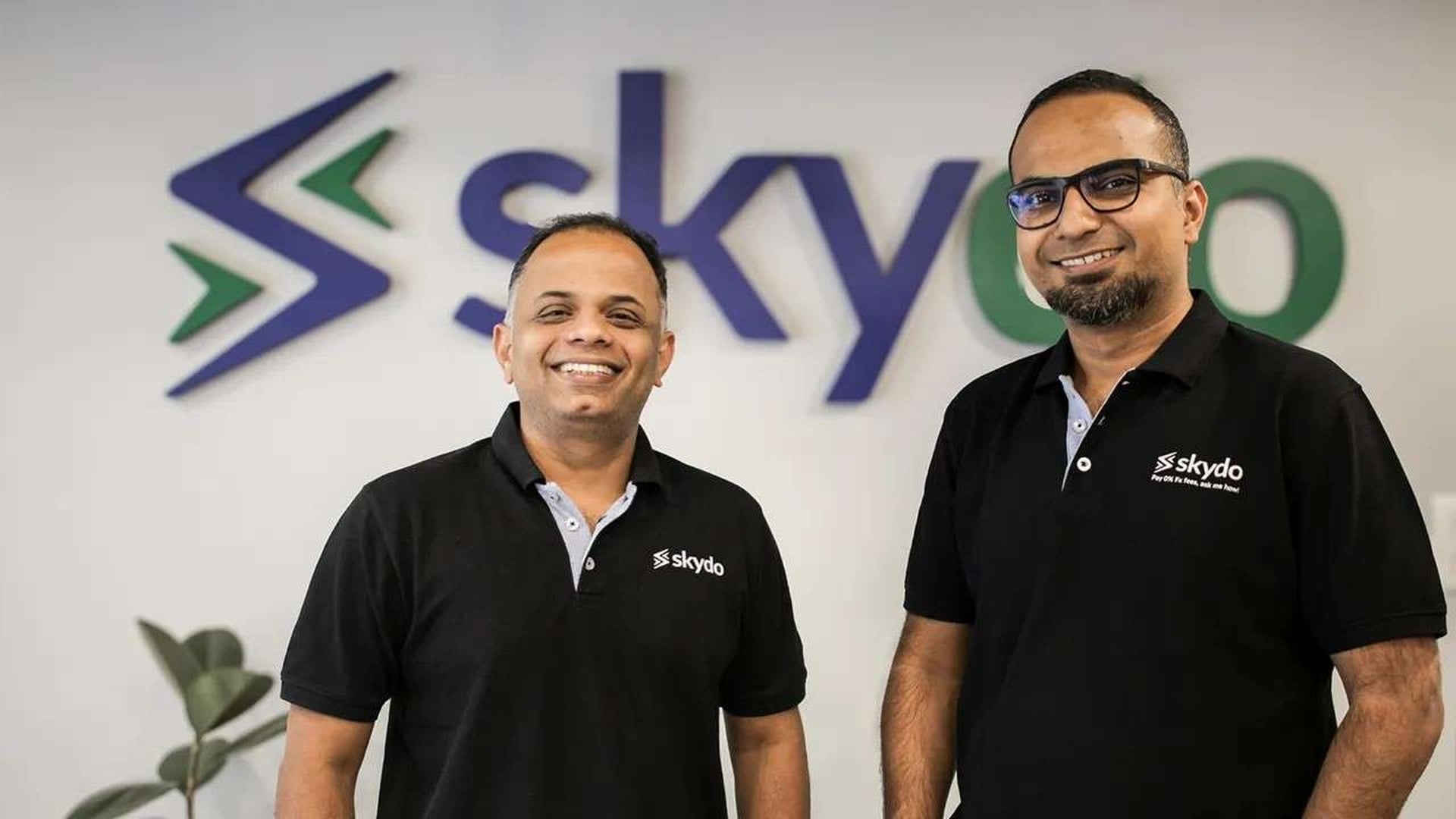 Skydo co-founders standing in front of the Skydo logo at the company office