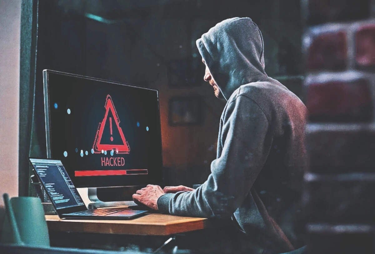 Hooded hacker at a computer showing a hacked warning, representing cyberattacks on NBFCs