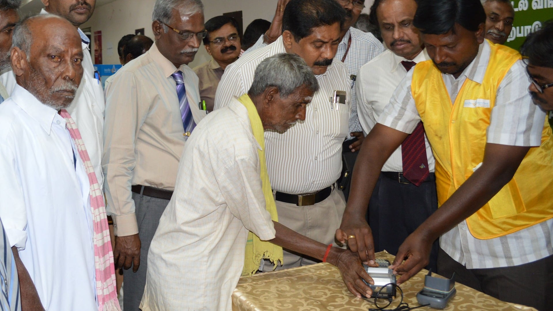 A rural customer authenticates a cash withdrawal on a biometric micro-ATM device operated by a banking correspondent