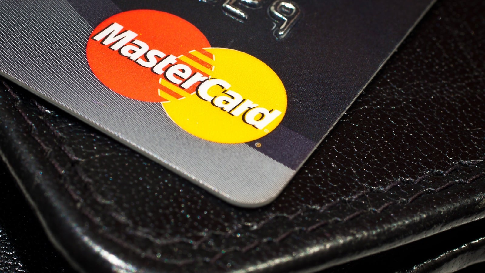 A Mastercard-branded payment card resting on a leather wallet
